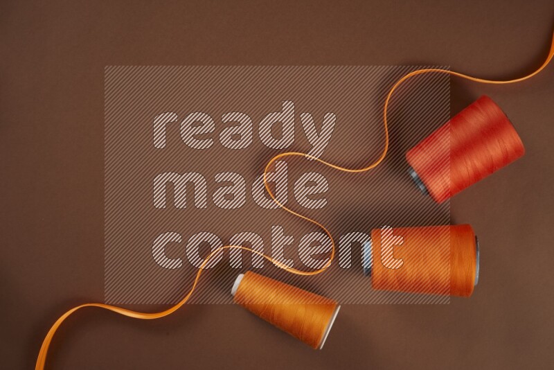 An orange collection of sewing and tailoring tools arranged on a brown background
