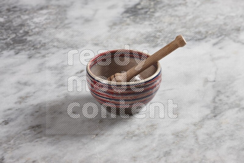 Multicolored pottery bowl with wooden honey dipper in it on grey marble background