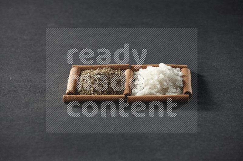 مربعان من أعواد القرفة ممتلئان بالملح الأبيض وحبوب الكمون علي خلفية سوداء