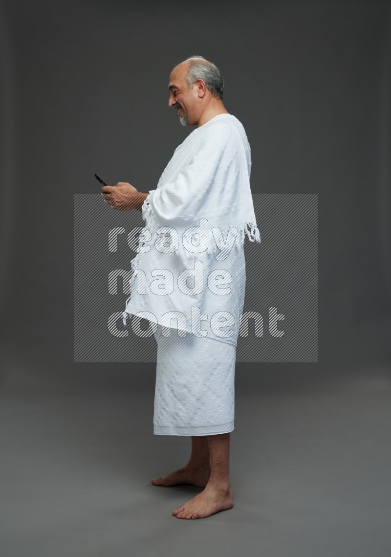 A man wearing Ehram Standing texting on phone on gray background