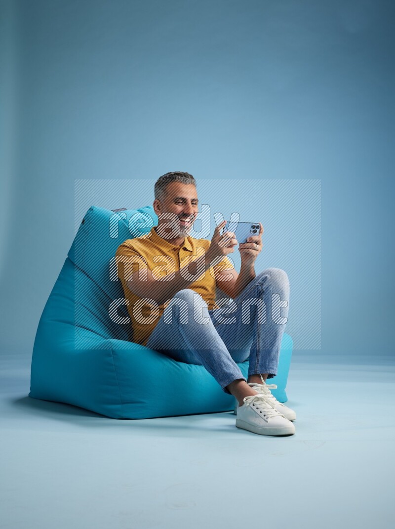 A man sitting on a blue beanbag and texting on phone