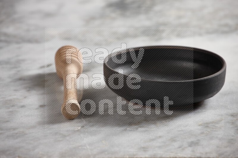 Black pottery bowl with wooden honey dipper on the side on grey marble background