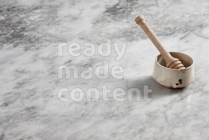 Beige pottery bowl with wooden honey dipper in it on grey marble background