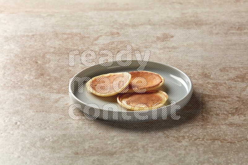 Three stacked plain mini pancakes in a blue plate on beige background