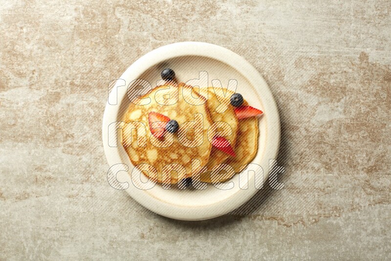 Three stacked mixed berries pancakes in a beige plate on beige background