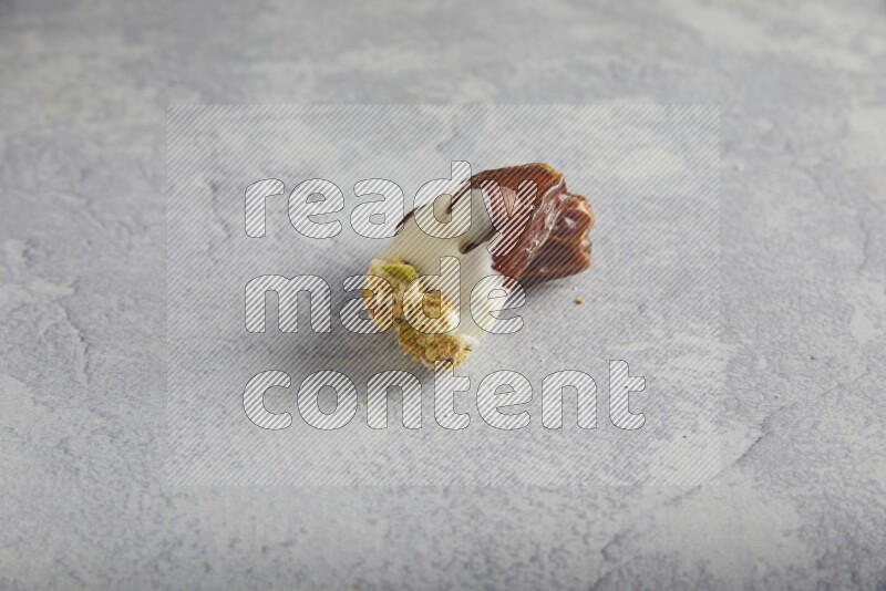 Hazulnut stuffed date covered with white chocolate and crushed peanuts & pistachios on light grey background