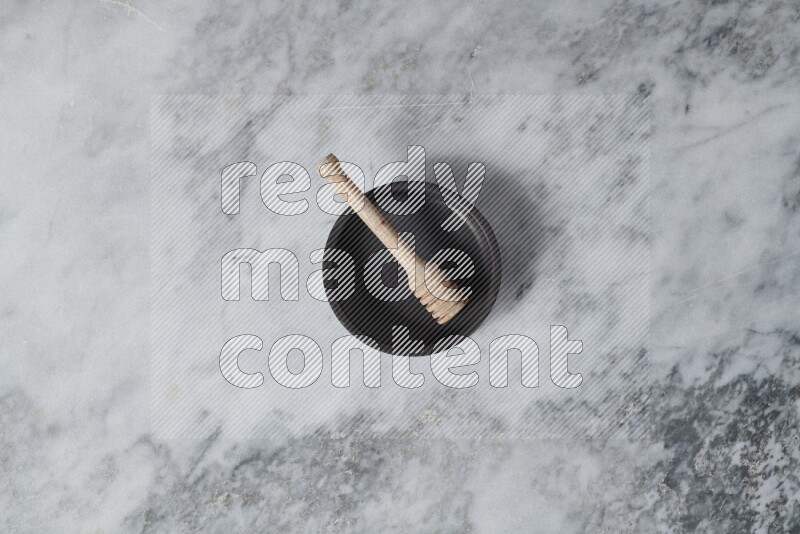 Black pottery oven plate with wooden honey dipper in it on grey marble background