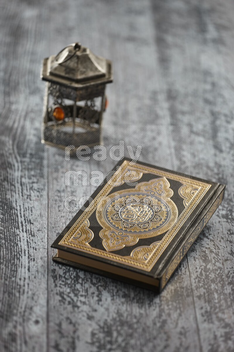 A silver lantern with different drinks, dates, nuts, prayer beads and quran on grey wooden background
