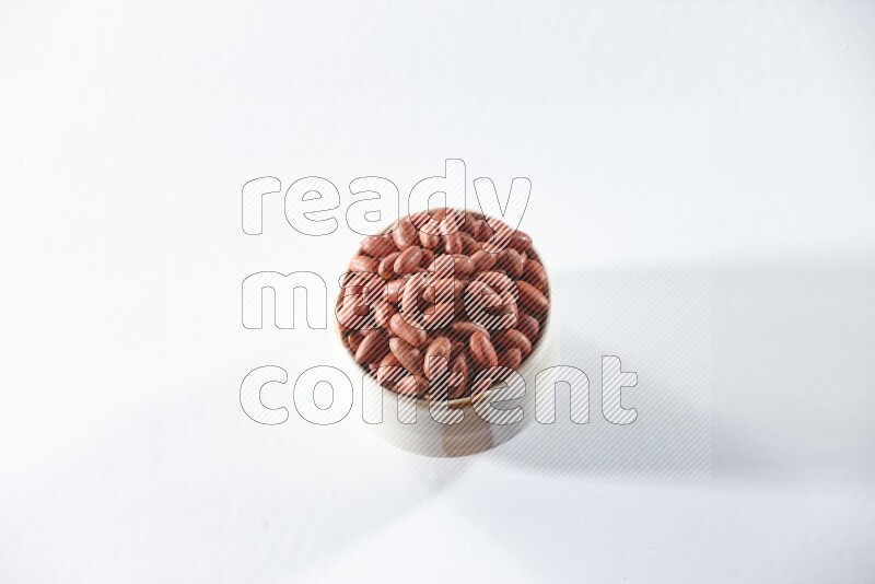 A beige ceramic bowl full of red skin peanuts on a white background in different angles