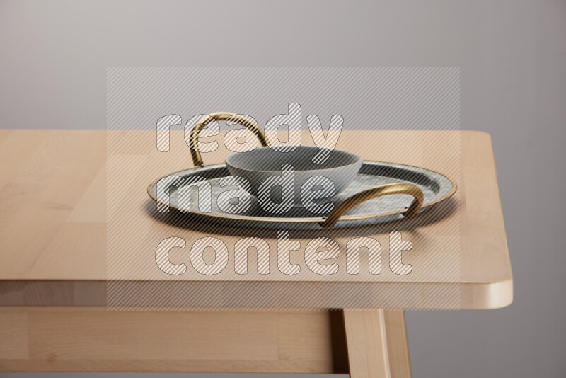 grey bowl placed on a rounded stainless steel tray with golden handels on the edge of wooden table