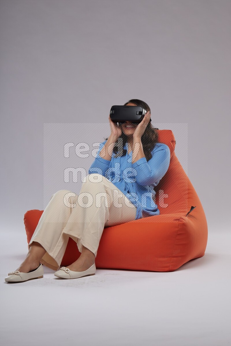 A woman sitting on an orange beanbag and gaming with VR