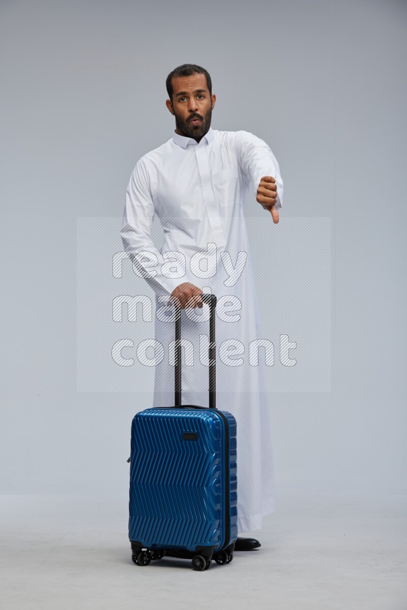 Saudi man wearing thob standing holding Travel bag on Gray background