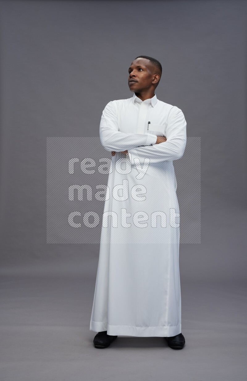 Saudi man wearing thob standing with crossed arms on gray background