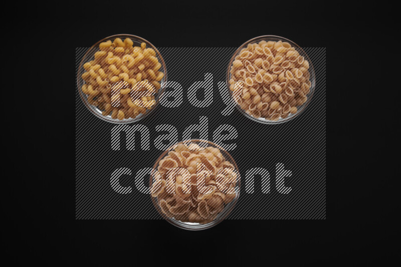 Different pasta types in glass bowls on black background
