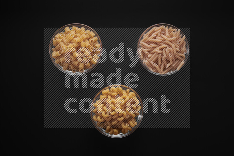 Different pasta types in glass bowls on black background