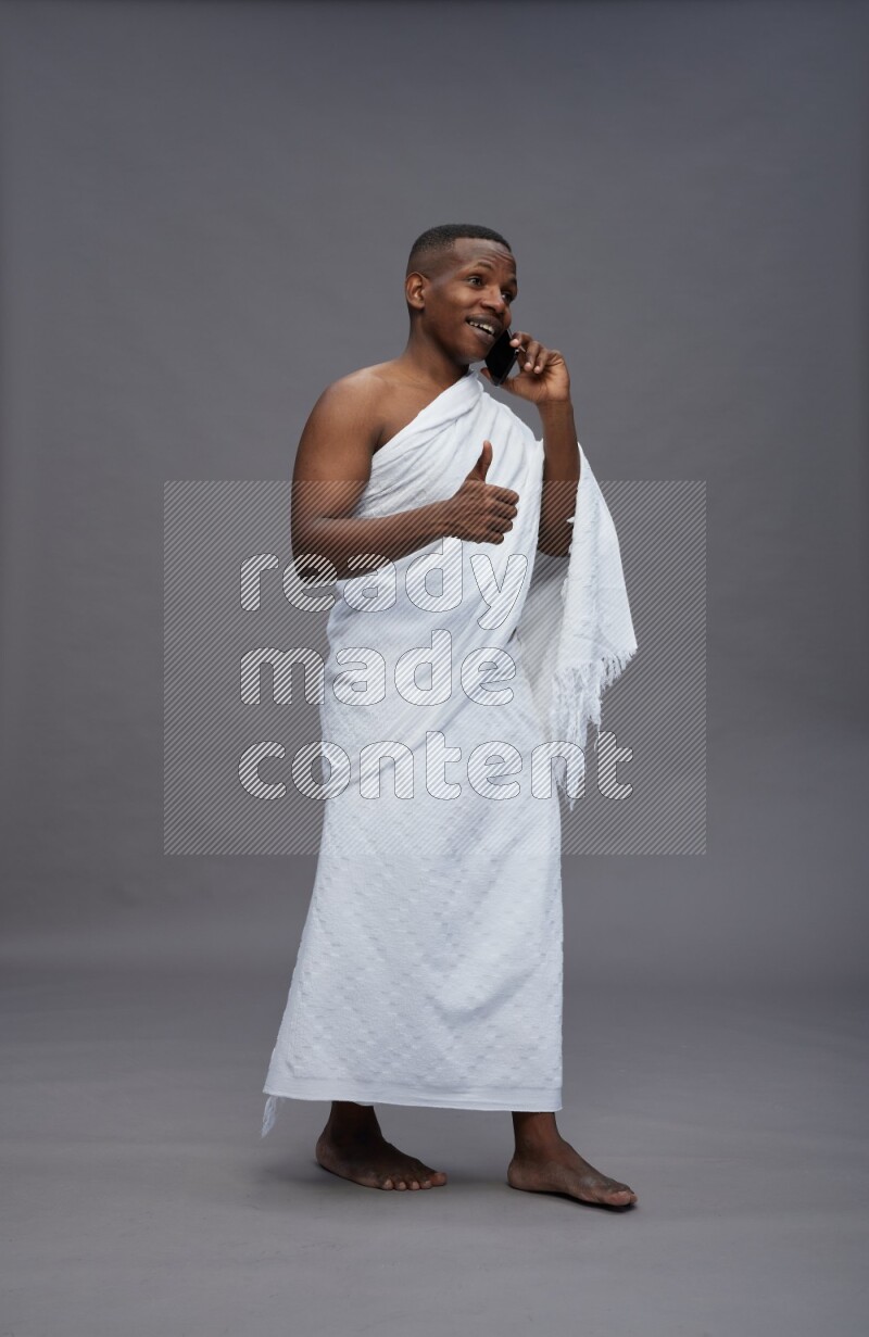 A man wearing Ehram Standing talking on phone on gray background