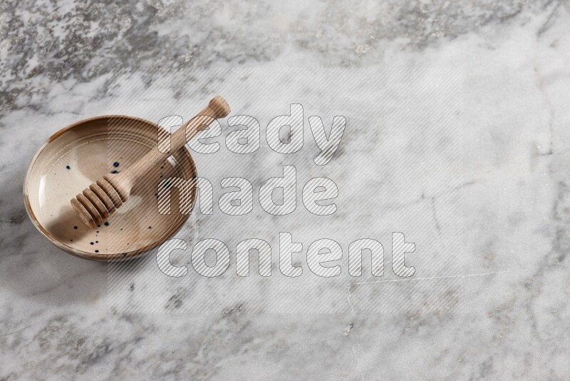 Multicolored pottery bowl with wooden honey dipper in it on grey marble background