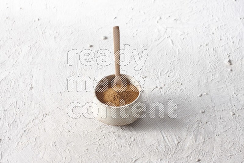 Ceramic beige bowl full of cinnamon powder with a wooden spoon on a textured white background