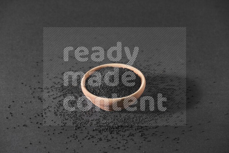 وعاء خشبي ممتلئ ببذور حبة البركة محاط ببعض البذور علي خلفية سوداء