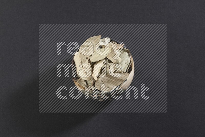 وعاء فخاري متعدد الألوان ممتلئ بأوراق الغار المجففة على أرضية سوداء