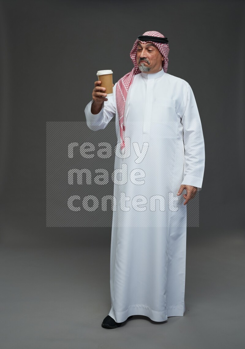 Saudi man with shomag Standing holding paper cup on gray background