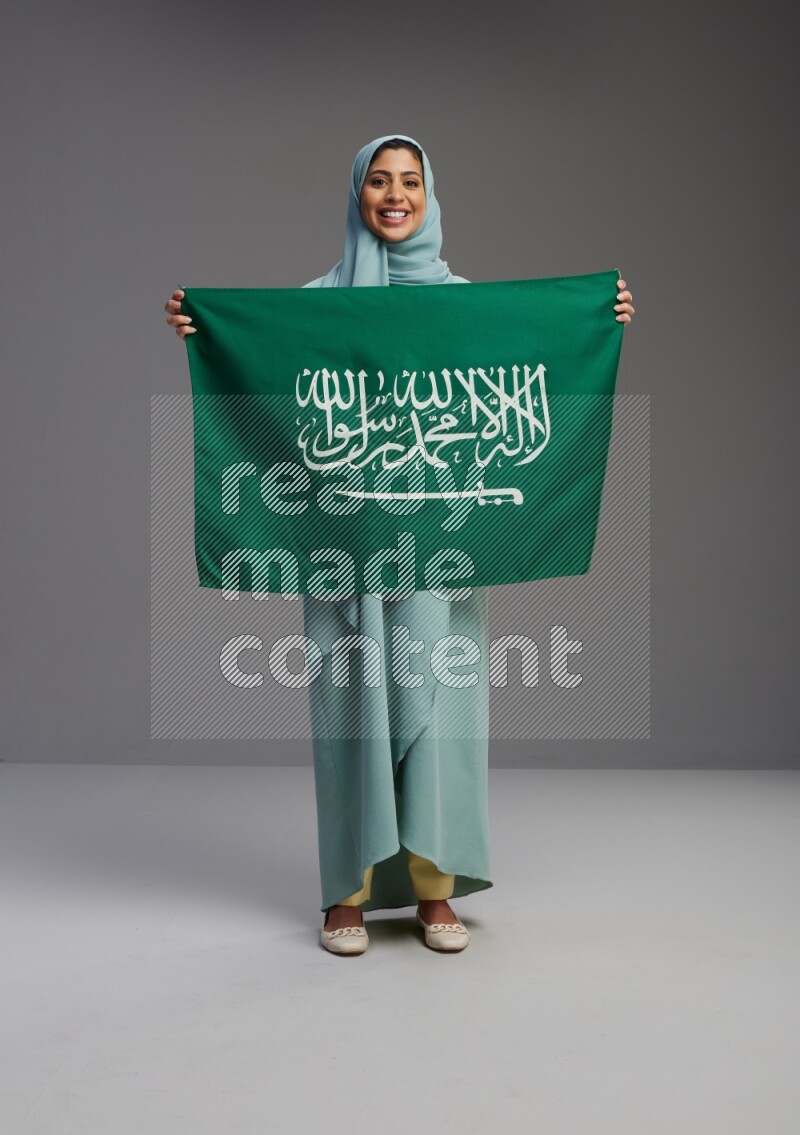 Saudi Woman wearing Abaya standing holding Saudi flag on Gray background