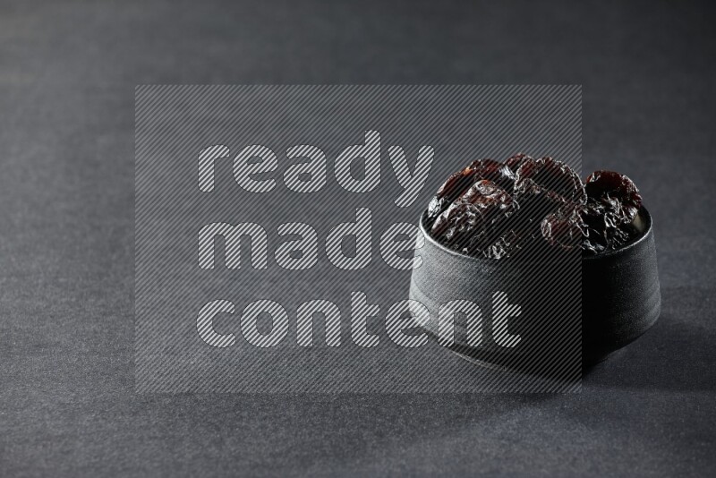 A black pottery bowl full of dried plums on a black background in different angles