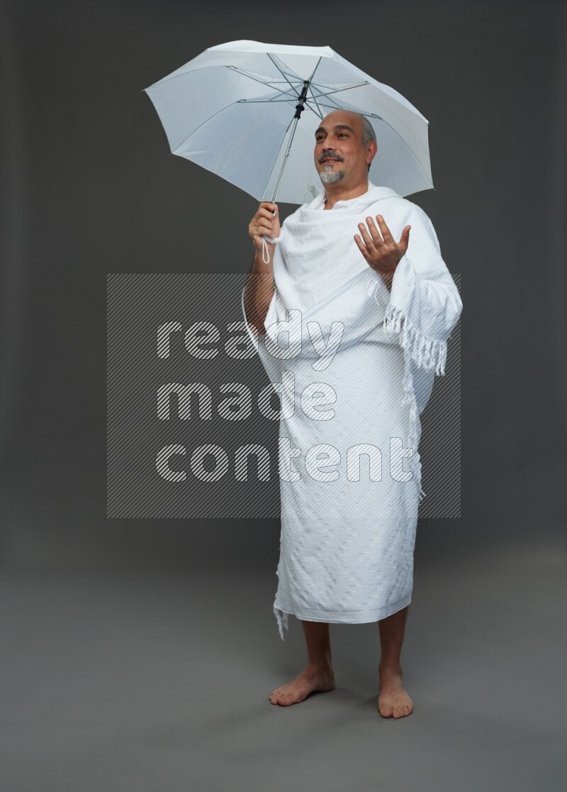 A man wearing Ehram Standing holding umbrella on gray background