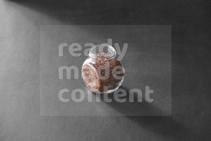 A glass spice jar full of flax on black flooring