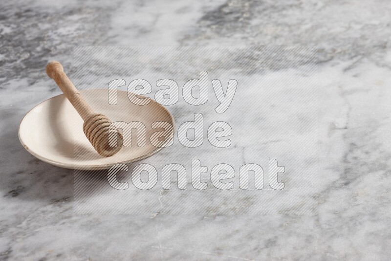 Beige pottery plate with wooden honey dipper in it on grey marble background