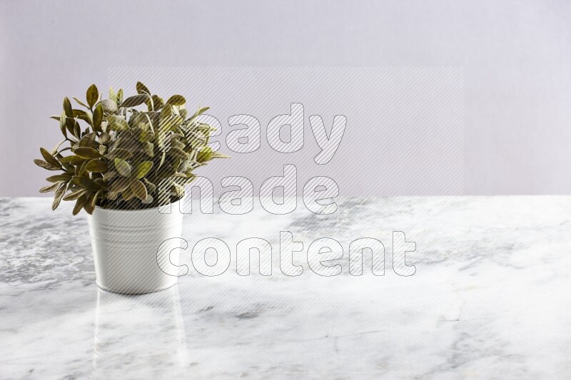 Green artificial plant in white pot on light grey marble background