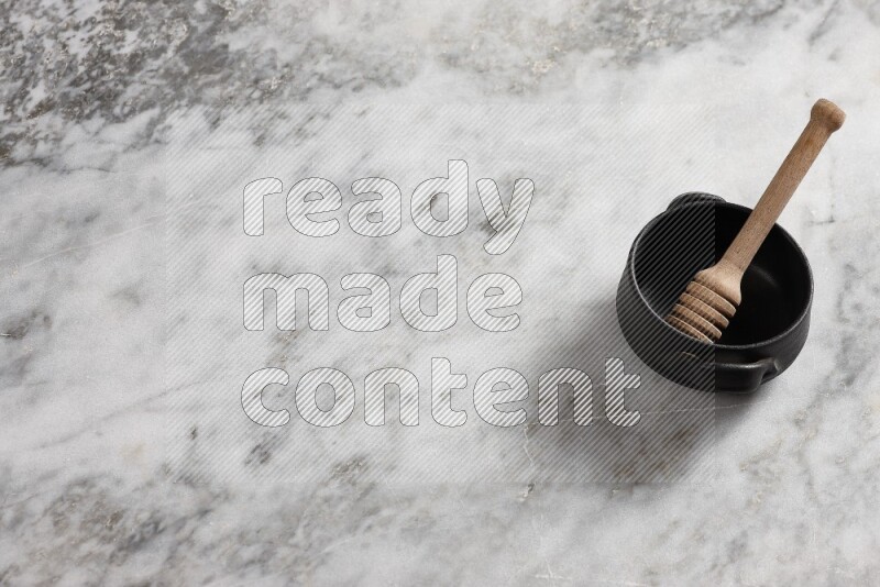 Black pottery bowl with wooden honey dipper in it on grey marble background