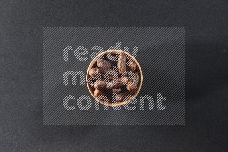 A wooden bowl full of dried dates on a black background in different angles