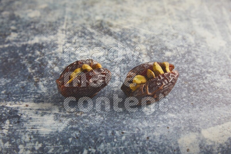 two pistachios stuffed madjoul dates on a rustic blue background