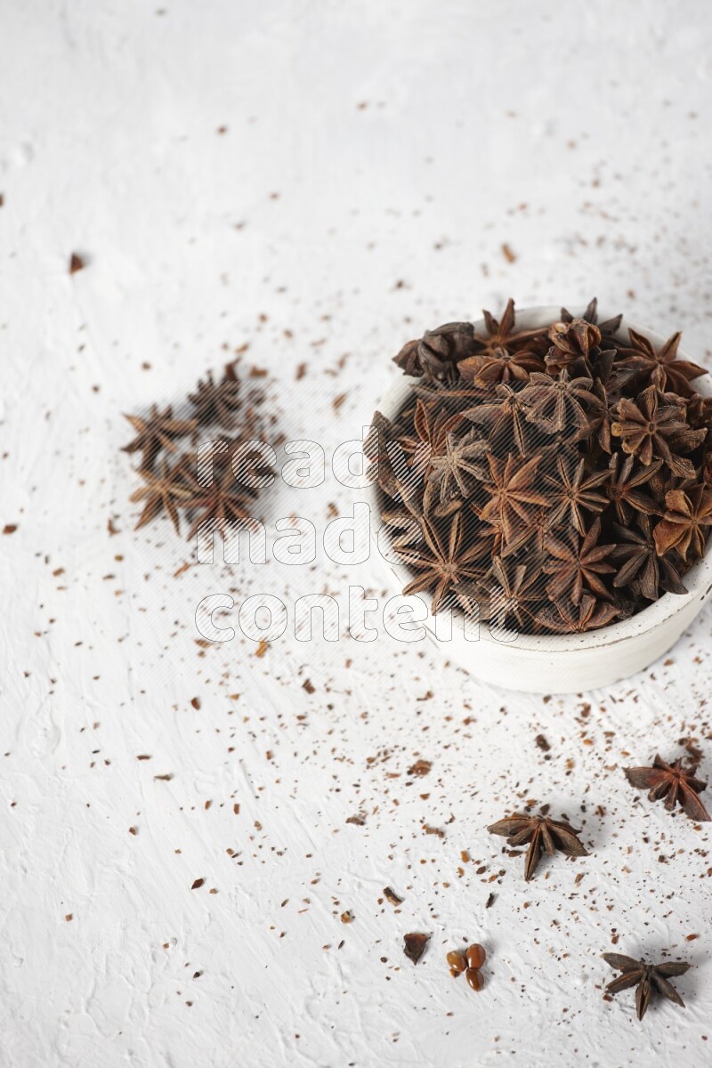 Star Anise in a white bowl and more of it sprinkled on white background