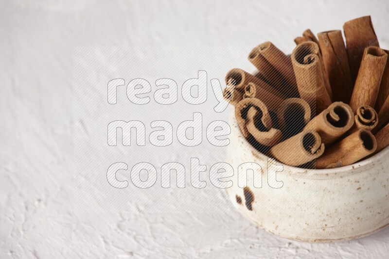 Cinnamon sticks in a beige bowl on a white background