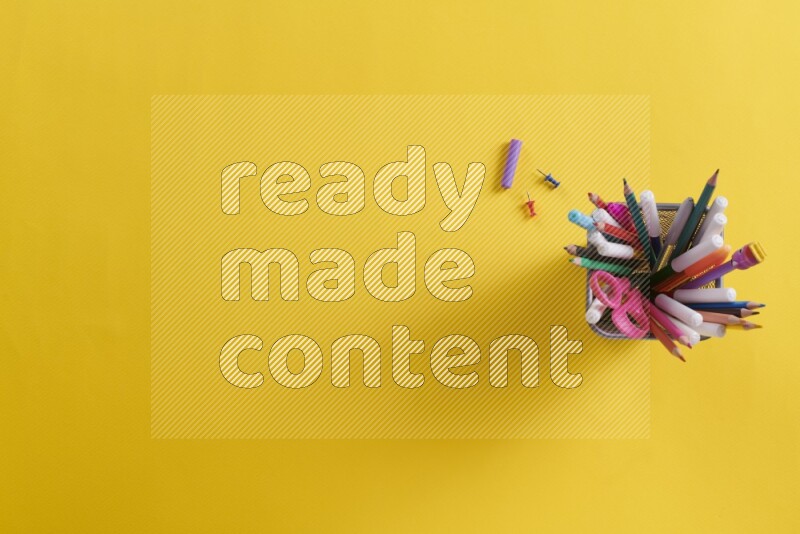 Pens, pencils and school supplies in a metal pen holder on yellow background