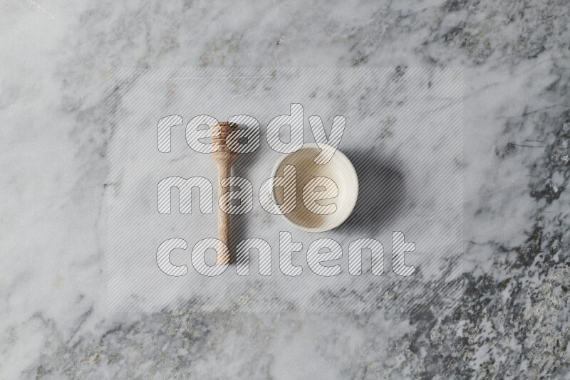 White pottery bowl with wooden honey dipper on the side on grey marble background