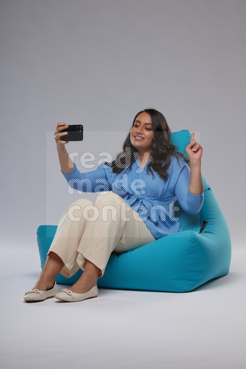 A woman sitting on a blue beanbag and taking selfie