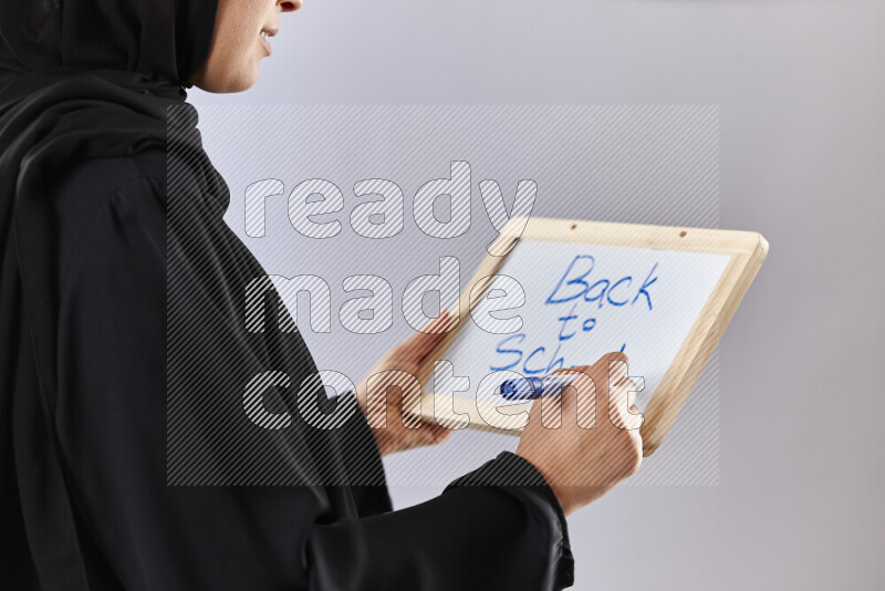 A woman in abaya holding books and a board in different positions (back to school)
