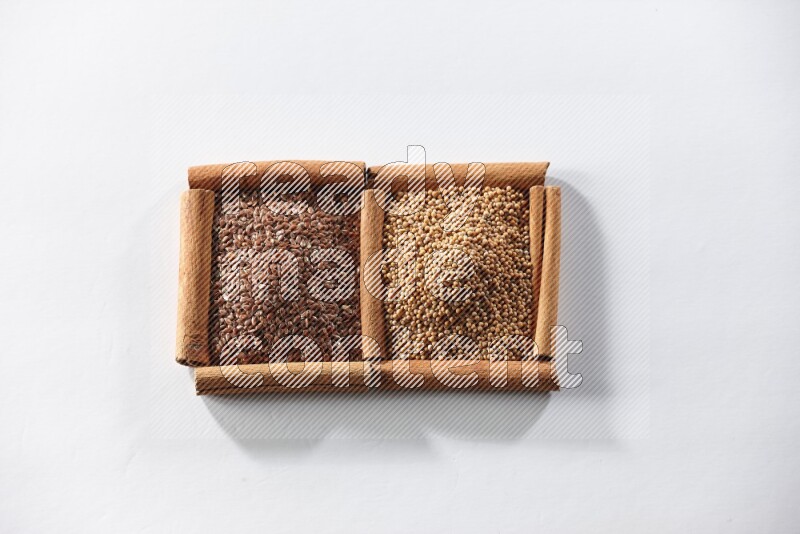 مربعان من أعواد القرفة ممتلئان بحبوب الخردل وبذور الكتان علي خلفية بيضاء