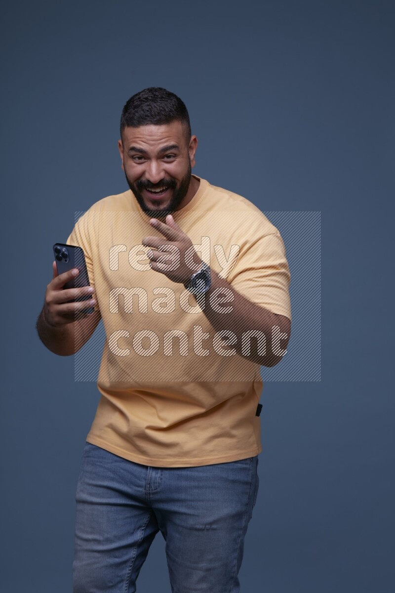 A man Pointing at a Smartphone on Blue Background wearing Orange T-shirt