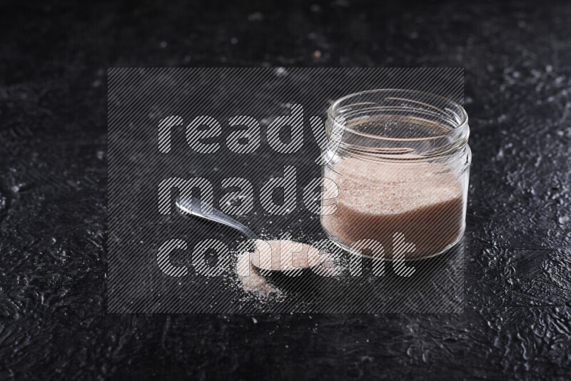 A glass jar full of fine himalayan salt on black background