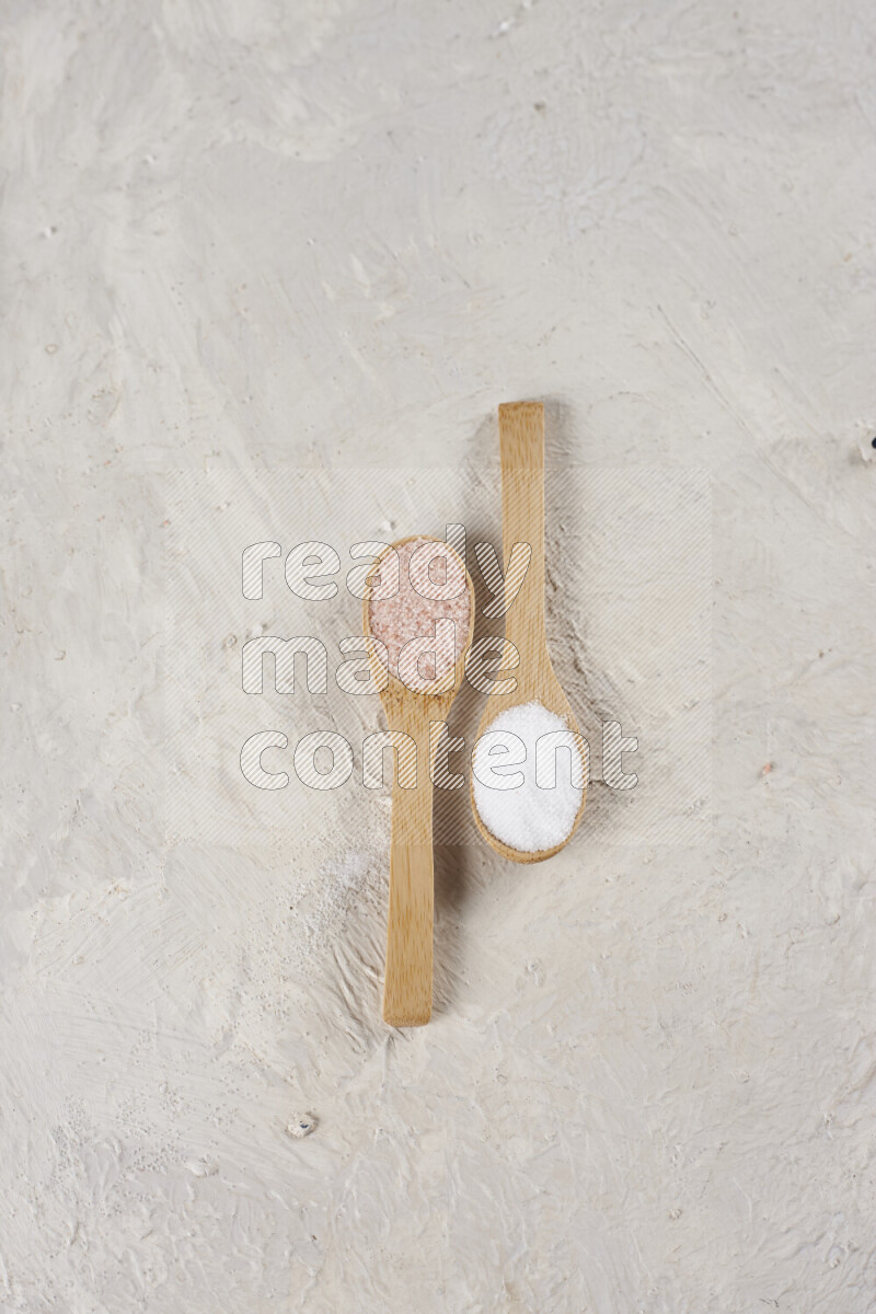2 wooden spoons filled with fine and coarse salt on white background