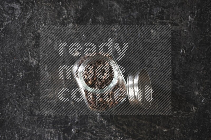 وعاء بهارات زجاجي ممتلئ بحبوب القرنفل على أرضية سوداء