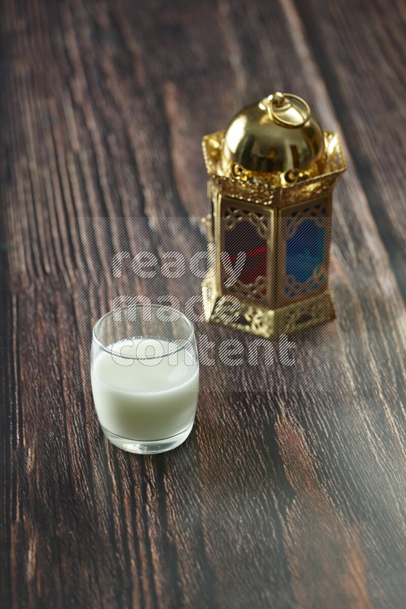 A golden lantern with different drinks, dates, nuts, prayer beads and quran on brown wooden background