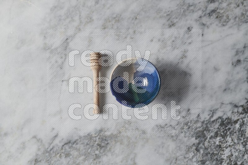 Multicolored pottery bowl with wooden honey dipper on the side on grey marble background