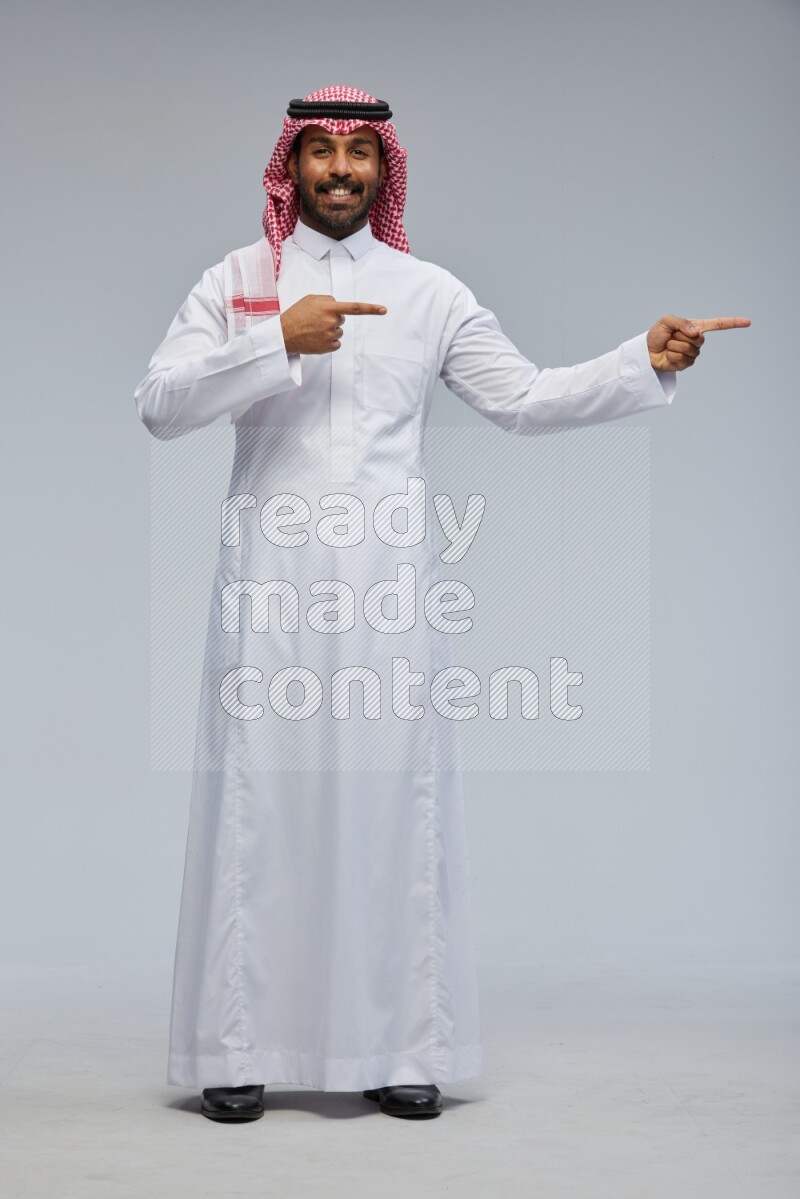 Saudi man Wearing Thob and shomag standing interacting with the camera on Gray background