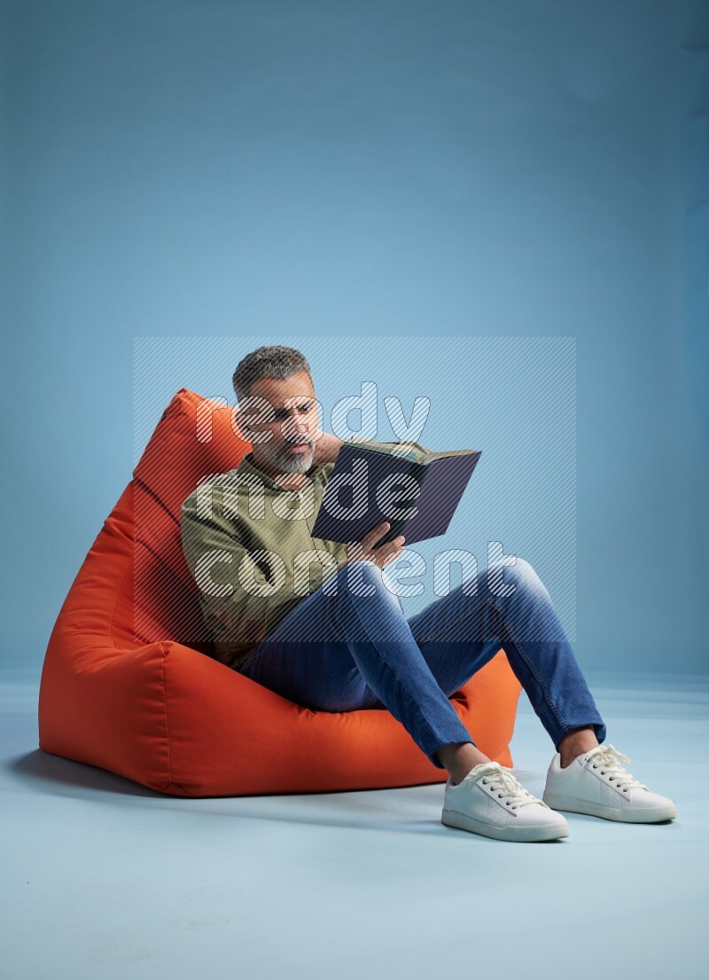 A man sitting on an orange beanbag and reading a book