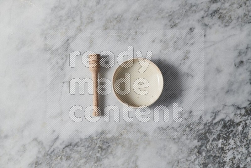 Beige pottery bowl with wooden honey dipper on the side on grey marble background